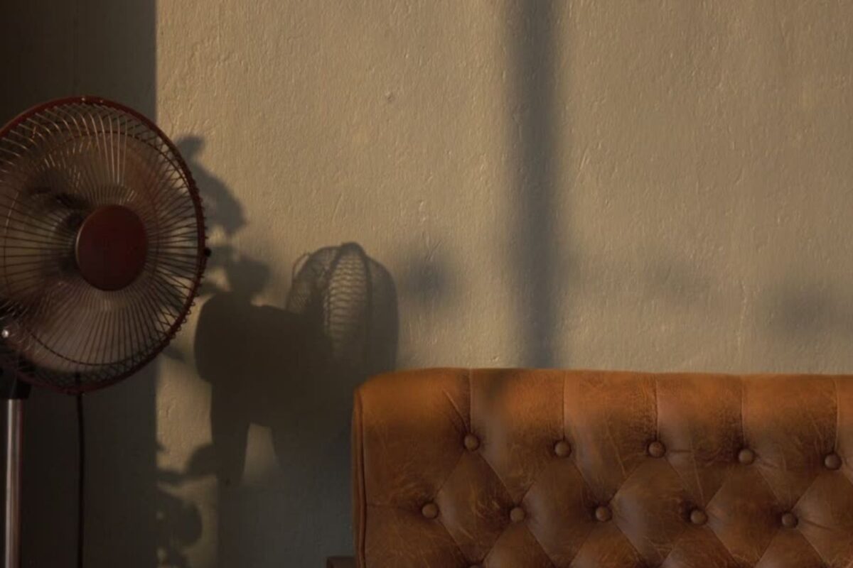 Ventilador de pedestal al lado de un sofá de piel marrón