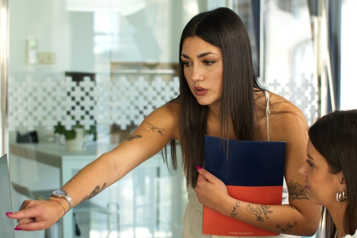 Una trabajadora de Máis Enerxía señalando a la pantalla del ordenador de una compañera mientras le explica algo en la oficina