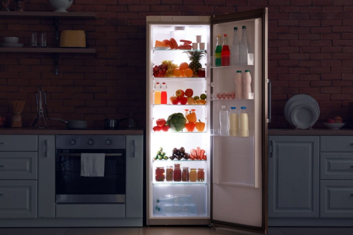 Frigorífico abierto con luz interior encendida en cocina a oscuras.