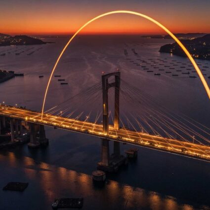 Imagen del Puente de Rande y de la Ría de Vigo al atardecer con las luces iluminadas. Un haz de luz recorre el puente.