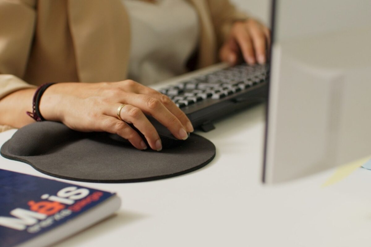 En la imagen se observan las mano de una de las personas del equipo Atención a Clientes de Máis Enerxía Galega sobre el ratón y teclado de su ordenador. También aparece en la imagen una libreta con el logotipo de la compañía.